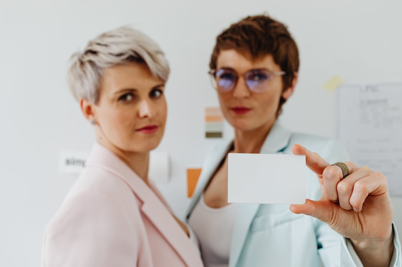 Two women in blazers presenting a blank business card, ideal for corporate themes.